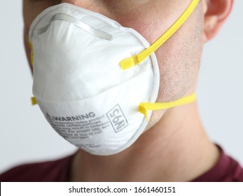 A man is shown wearing a protective N95 white respirator dusk mask up close, set against a white background during the day.