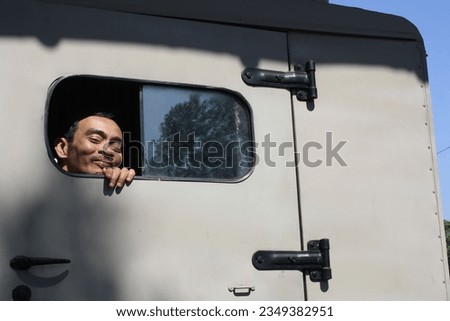 a man shows his face through the window of an army car in broad daylight