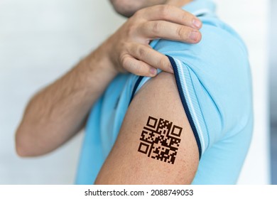 The man shows his shoulder with a qr code, a confirmation of the vaccination against the covid 19 coronavirus. Temporary tattoo.