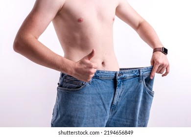 A Man Shows How He Lost Weight, Big Jeans On A Light Background, The Concept Of Losing Weight