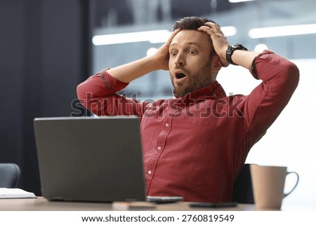 Man Shows Surprise While Working at Desk With Laptop During Daytime in Office Setting