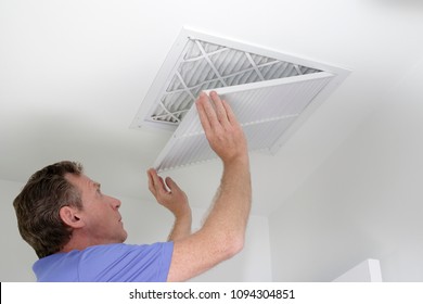 Man shutting grill of HVAC, heating ventilating and cooling after replacing the air filter. Closing ceiling grill after replacing an air filter in the ceiling.
