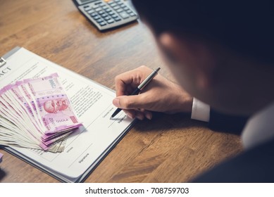 A man signing an agreement with Indian Rupees money on top of paper after a calculation has been done