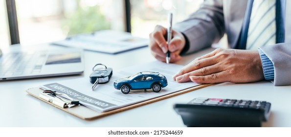 Man signing car insurance document or lease paper. Writing signature on contract or agreement. Buying or selling new or used vehicle. Car keys on table. Warranty or guarantee. Customer or salesman. - Shutterstock ID 2175244659