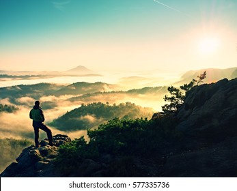 Man silhouette climbing high on cliff. Hiker climbed up to peak enjoy view. Man  watch over misty and foggy morning valley in morning Sun. 