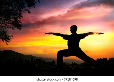 Man Silhouette Doing Virabhadrasana II Warrior Pose With Tree Nearby Outdoors At Sunset Background