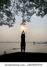 Man silhouette doing yoga and surya namaskar exercise near Lake during sunrise.