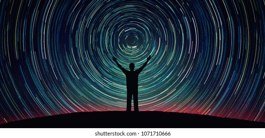 Man silhouette on a night sky background with bright stars trails. Man watching the stars. Science, education and religion team concept background. Elements of this image furnished by NASA.