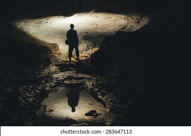 Man Silhouette Reflecting In Water In Dark Cave