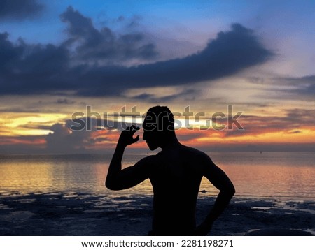 A man in silhouette stand on a beautiful beach with their hands raised against an orange sky background. Sunset in Indonesia