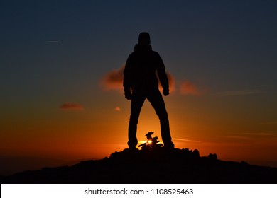 Man silhouette standing on the mountain peak while orange sunset. Strong, powerfull, successful man with his hands in fist. Outdoor background. - Powered by Shutterstock