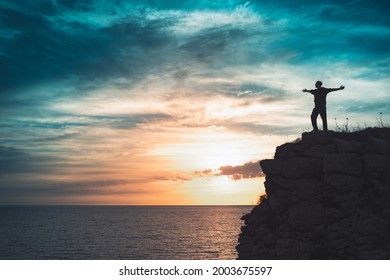 Man silhouette stands on the edge of the abyss and looks the sea with beautiful colorful sky.