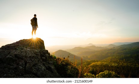 Man silhouette stay on sharp rock peak the view of sunset over an autumn forest in deep velly bellow. Enjoy moment ot of people
