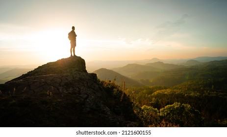 Man silhouette stay on sharp rock peak the view of sunset over an autumn forest in deep velly bellow. Enjoy moment ot of people