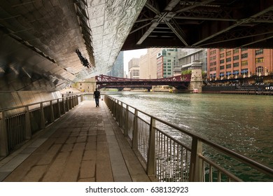 Man In Silhouette Strolling On Chicago River Walk Under A Bridge