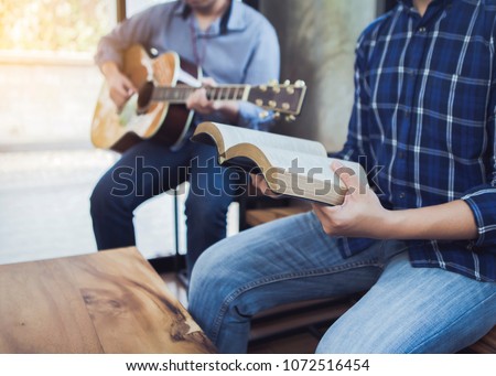 a man sing a song from hymn book while his friends playing guitar indoor