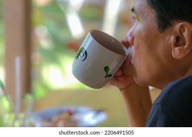 Man Sipping A Cup Of Hot Coffee In The Morning Over Blurry Background