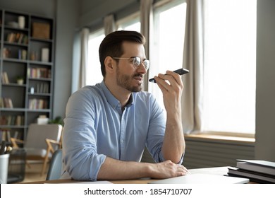 Man sit at desk at home office room holding smart phone communication device using loudspeaker answering to incoming call, leave voice audio message to client remotely. Virtual assistant usage concept - Powered by Shutterstock