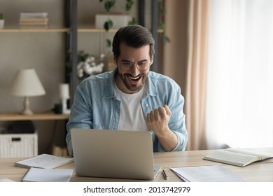 Man sit at desk read e-mail on laptop makes yes gesture feels happy. Male entrepreneur get great business news, celebrate career growth, advance. Achievement, win, moment of auction victory concept