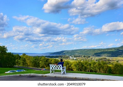 A Man Sit On Bench Overlooking The Valley Landscape Of Seneca Lake, Blue Clouds Sky, River And Mountain Forest. Amazing Summer Scene In Finger Lakes Region Of New York 