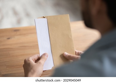 Man Sit At Table Opens Envelope With Letter Or Post Card Inside, Close Up View Over Male Shoulder. Paper Correspondence With Information, Bank Notification, Paperwork At Workplace, Invitation Concept