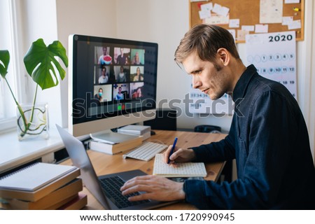 Man siting by desktop computer and making notes. Working remotely Young man having video call via computer in the home office. Stay at home and work from home concept. Managing business team meeting