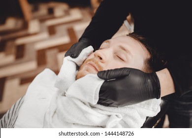 Man sits in barbershop chair and steam his face with hot towel in front of royal beard shaving razor. - Powered by Shutterstock