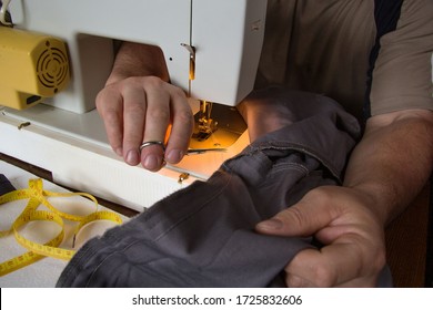 A Man Sits Behind A Sewing Machine And Makes A Line On His Trousers. He's Already Finished And Cuts Off The Thread With Scissors.