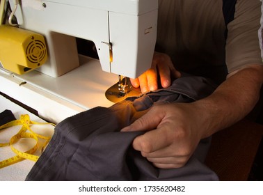 A Man Sits Behind A Sewing Machine And Makes A Line On His Trousers. He Has Not Yet Finished. He Is Sewing At Home.