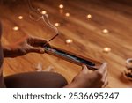 a man sits with his hands folded in prayer, holding an incense stick that emits smoke. In a warm, cozy atmosphere and several candles placed on a wooden floor, meditation