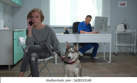 Man Sits With Husky And Talks On Phone In Cabinet Of Vet 