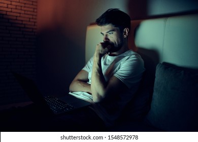 A man sits on the bed of an apartment building sleeping room watching TV