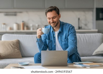 A man sits on a couch at home, working on a laptop while sipping a cup of coffee. He is wearing a casual blue shirt and smiling. He is working in a relaxed, comfortable setting. - Powered by Shutterstock