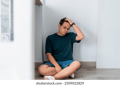 A man sits on the floor with a hand in his hair, displaying a depressed and thoughtful expression.