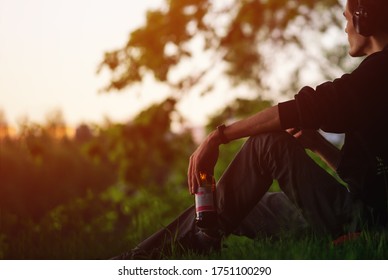 A Man Sits On The Grass In The Park, Listening To Music, Drinking Beer. Relax And Enjoy Your Life