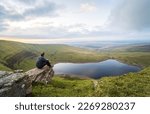 Man sits on a rock and looks at Llyn y Fan Fach lake. Brecon Beacons National Park. Black Mountain, Carmarthenshire, South Wales, the United Kingdom.