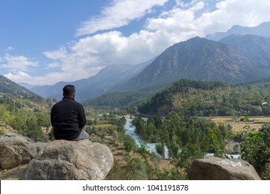 Man sits on the rock overlooking spectacular view of valley in Pahalgam Kashmir India.
