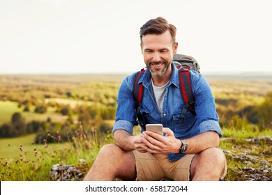 Man sits on the rock using mobile phone during summer trekking