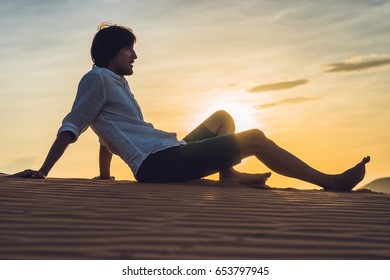 A man sits on the sand in the desert.