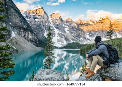 Man sits outdoor on big stone at beautiful Moraine Lake in Banff National Park, Alberta, Canada and enjoys the nature landscape view. Sunrise scene in valley of ten peaks. Blue sky with white clouds. - Powered by Shutterstock