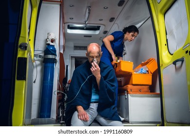 Man Sits With Oxygen Mask, Nurse In Uniform Packs Equipment In Medical Bag