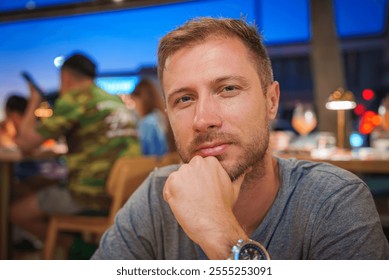 A man sits in a restaurant with a thoughtful expression, chin resting on hand. The background shows patrons in casual attire and warm table lamp lighting. - Powered by Shutterstock