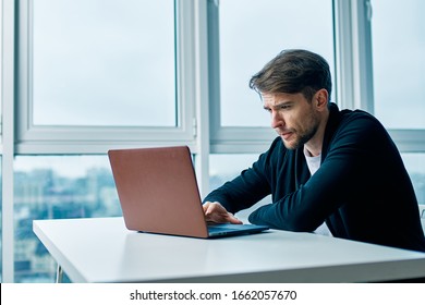 A Man Sits At A Table In Front Of Open Laptop Near The Window