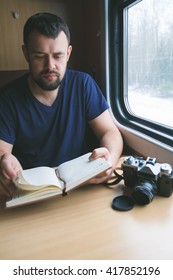 The man sits at a table in a train, looking into the notebook