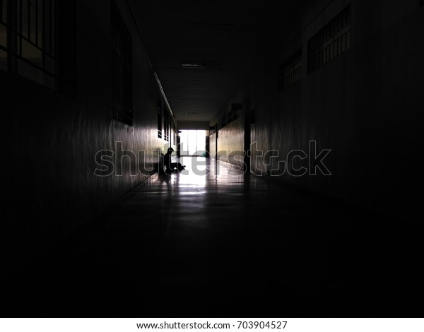 Man\
sitting alone in dark corridor with light at the\
end