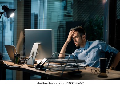 Man sitting alone in office late at night watching computer and solving problem working overhours. 