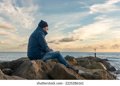 Man sitting alone on rocks looking at the sea. - Powered by Shutterstock