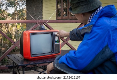 A Man Sitting Alone Watching Old TV Outside The House With Turning Old Television Knob