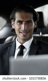 man sitting in the back-seat of a car, using his laptop