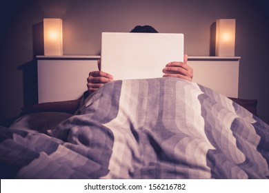 Man Is Sitting In Bed Behind His Laptop